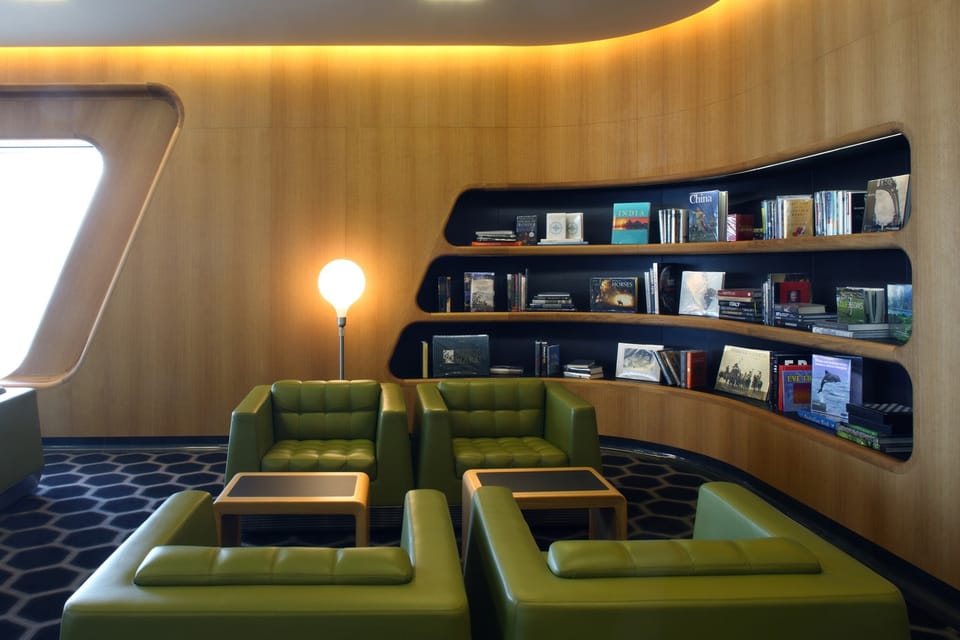 Reading corner with green armchairs and curved timber bookshelves in the Qantas Chairman's Lounge Sydney